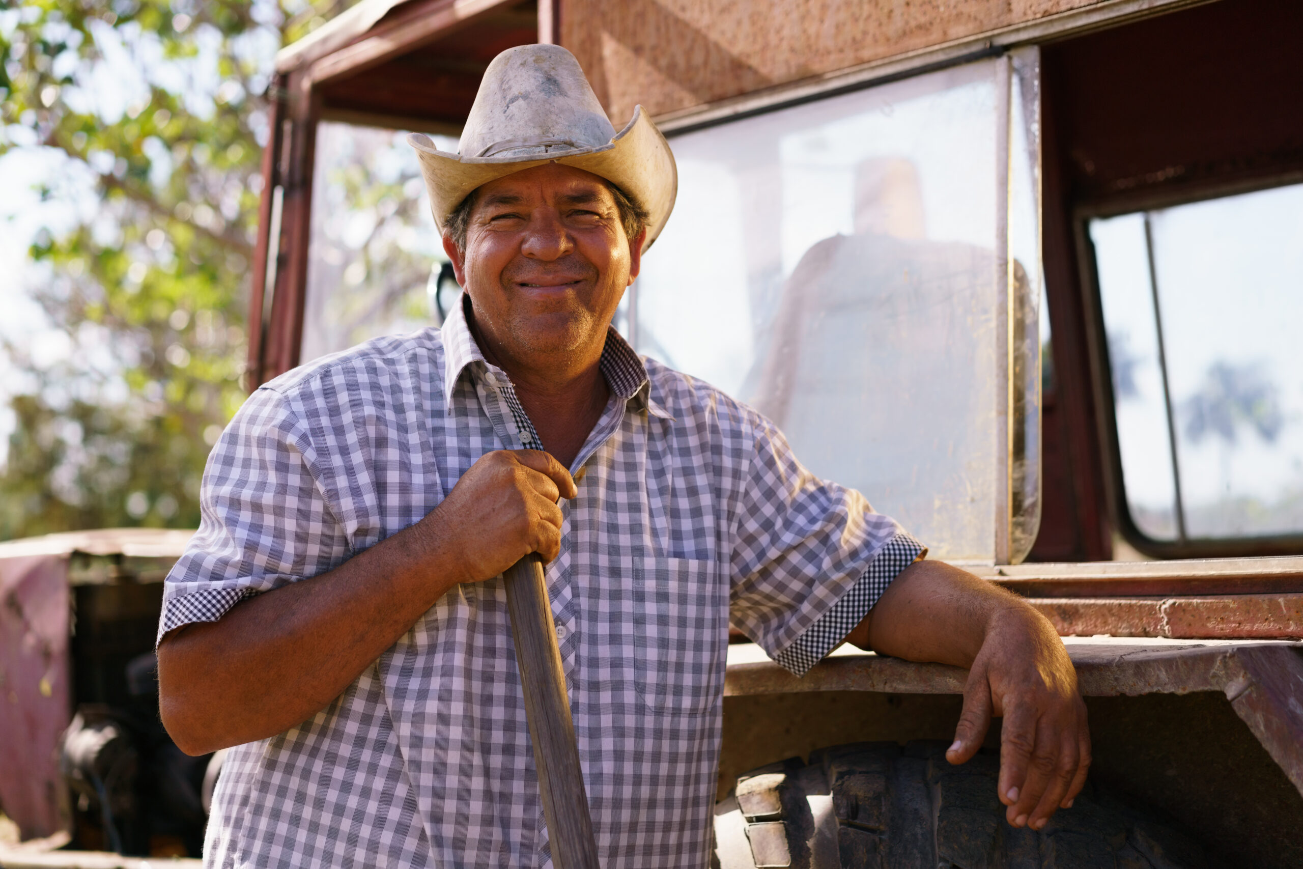 Happy male farmer leaning on tractor, smiling at camera