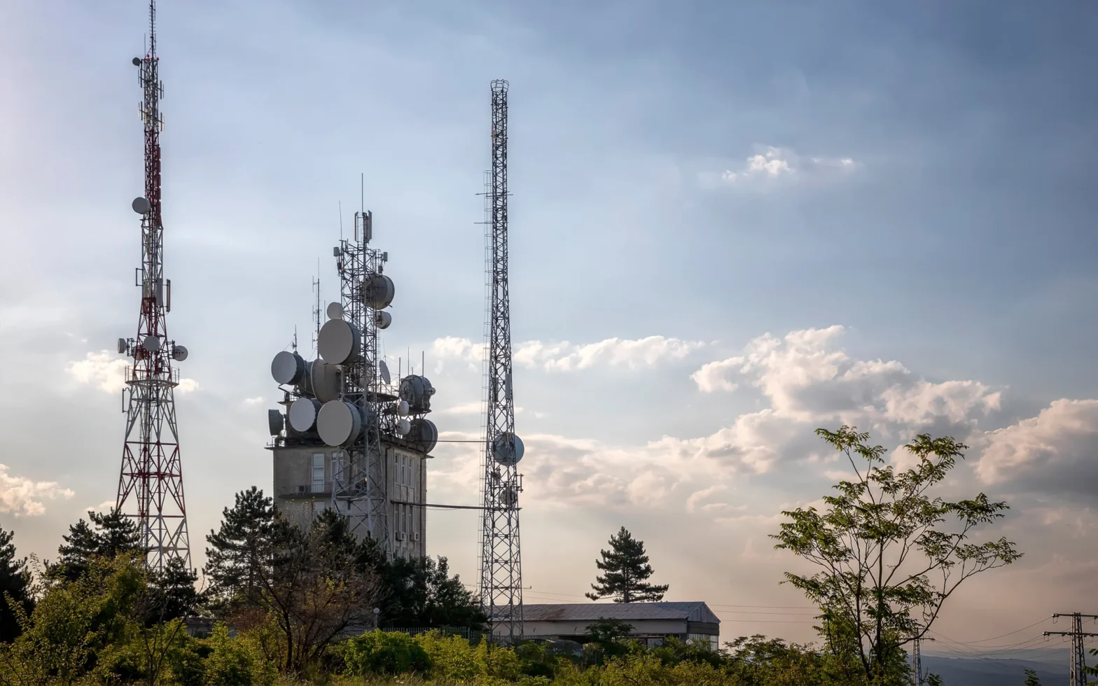Tall telecommunication towers with antennas and satellite dishes against a partly cloudy sky