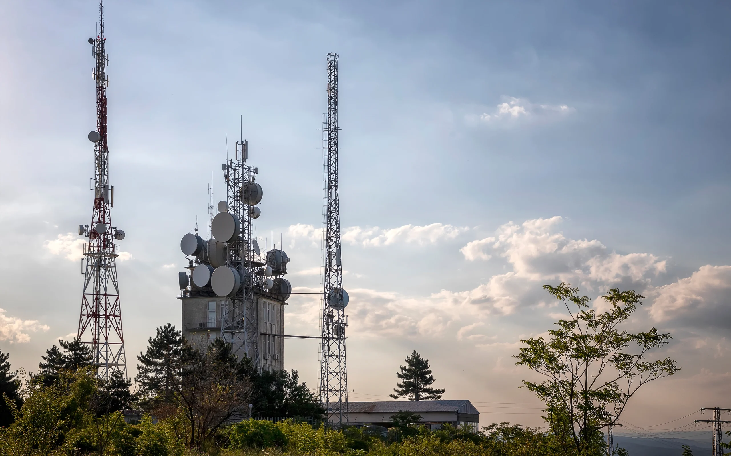 Tall telecommunication towers with antennas and satellite dishes against a partly cloudy sky