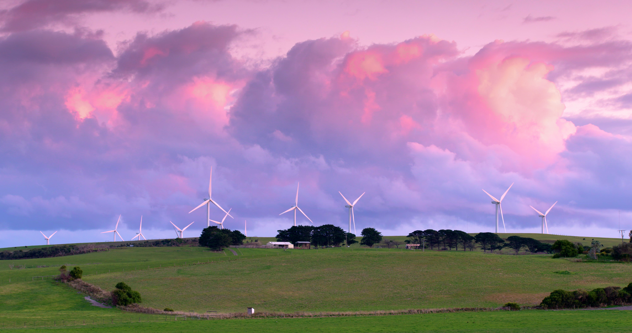 A landscape featuring wind turbines against a colorful sunset sky with soft clouds.