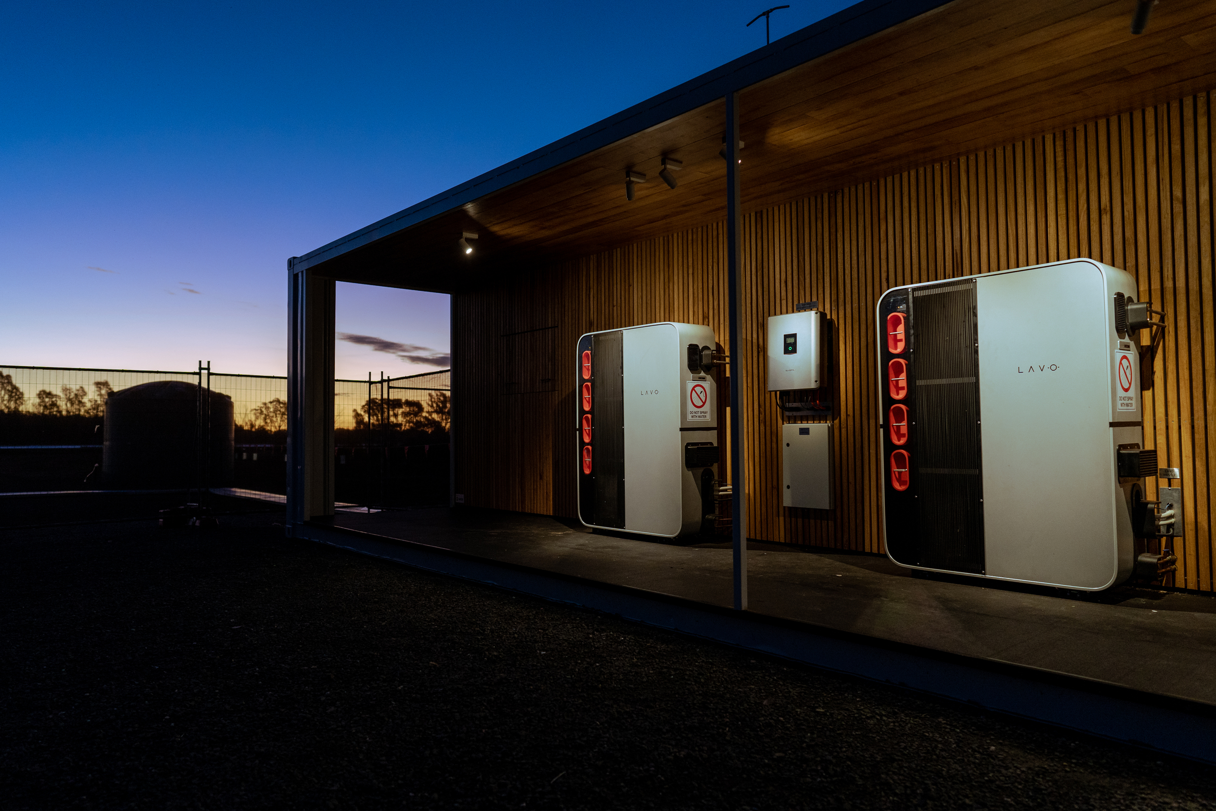 Two modern energy storage units installed on a wooden wall, illuminated against a twilight sky.
